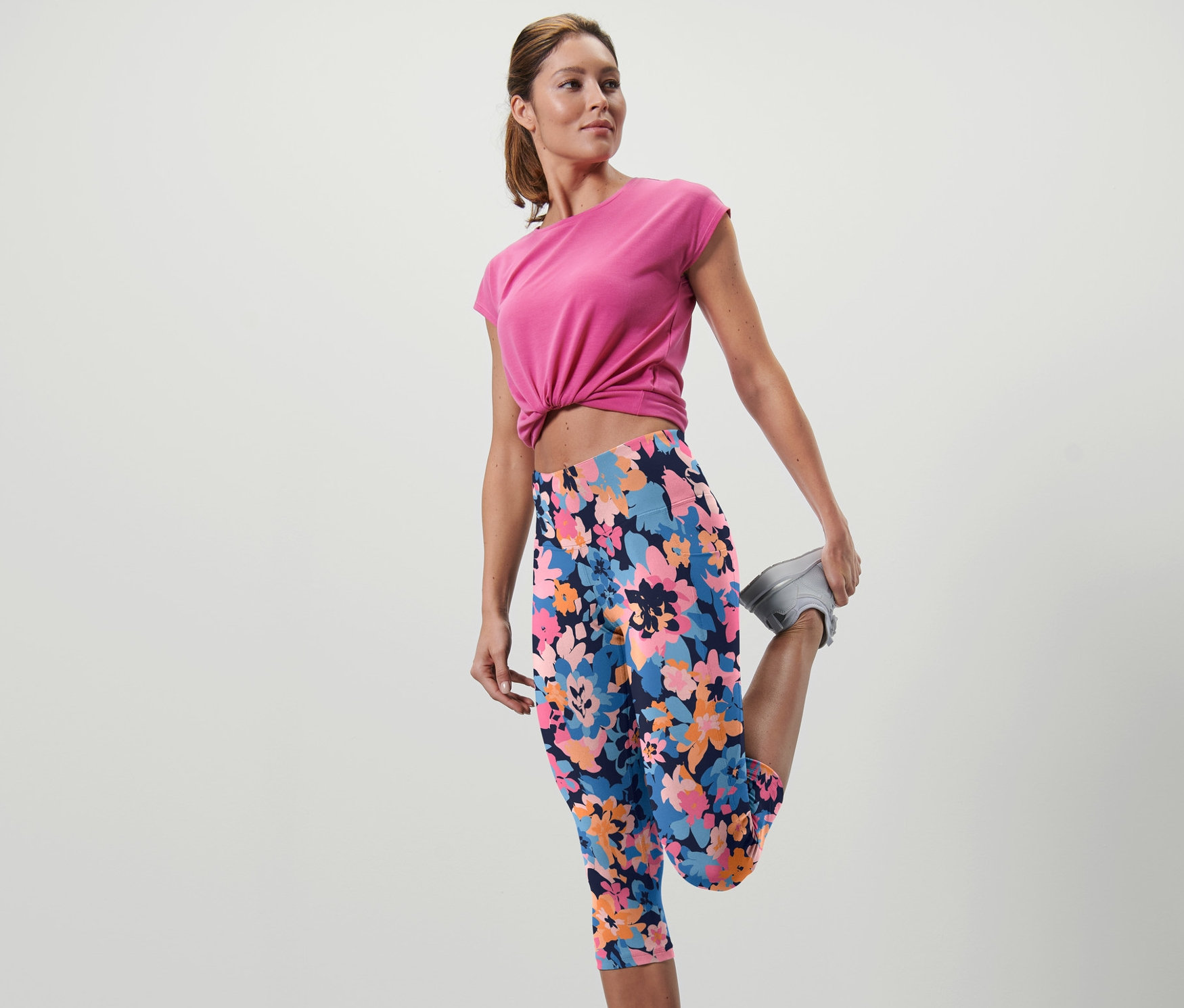 Kobieta rozciąga nogę w legginsach sportowych o długości 3/4 w kwiatowy wzór.