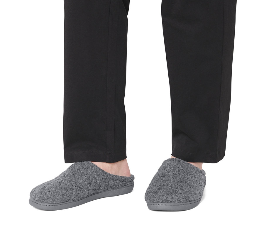 Stopy w czarnych spodniach i szarych kapciach.