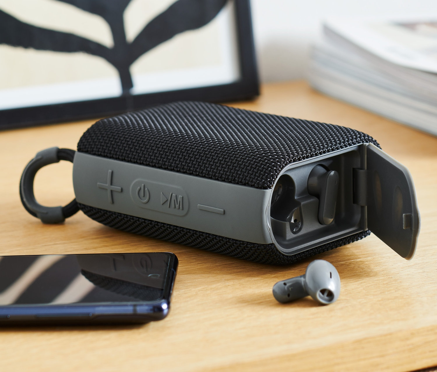 Czarny głośnik Bluetooth ze słuchawkami dousznymi na drewnianym stole.