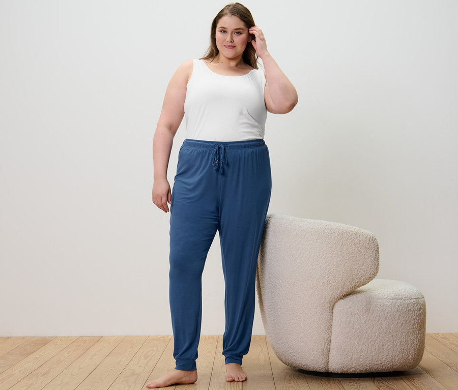 Kobieta stoi, ubrana w 2 podkoszulki granatowe i białe oraz spodnie od piżamy.