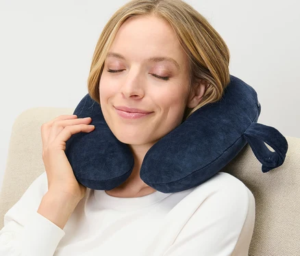 Kobieta siedzi w fotelu z granatową poduszką pod kark z pianki memory foam na szyi.