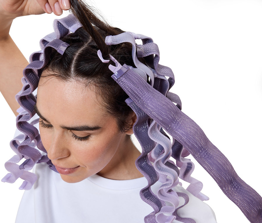 Kobieta nawija włosy na fioletowe wałki.