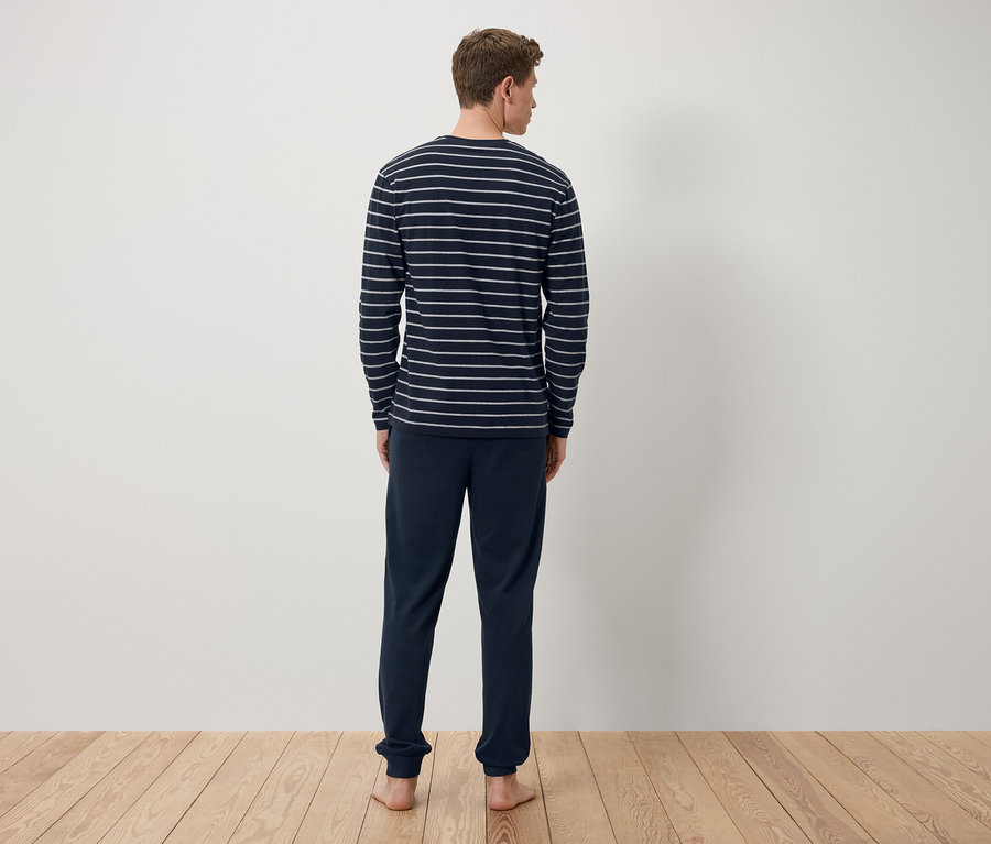 Mężczyzna tyłem do kamery ma na sobie granatową koszulkę z długim rękawem w paski i granatowe spodnie dresowe.