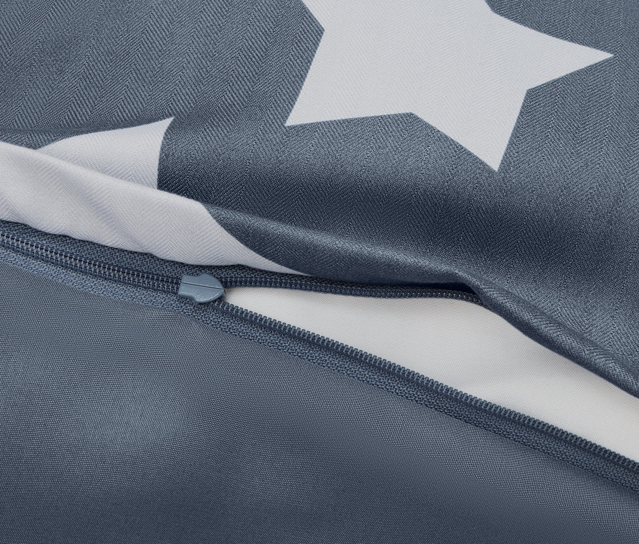 Zbliżenie na niebieską poszwę na kołdrę z białymi gwiazdami i częściowo rozpiętym zamkiem błyskawicznym.