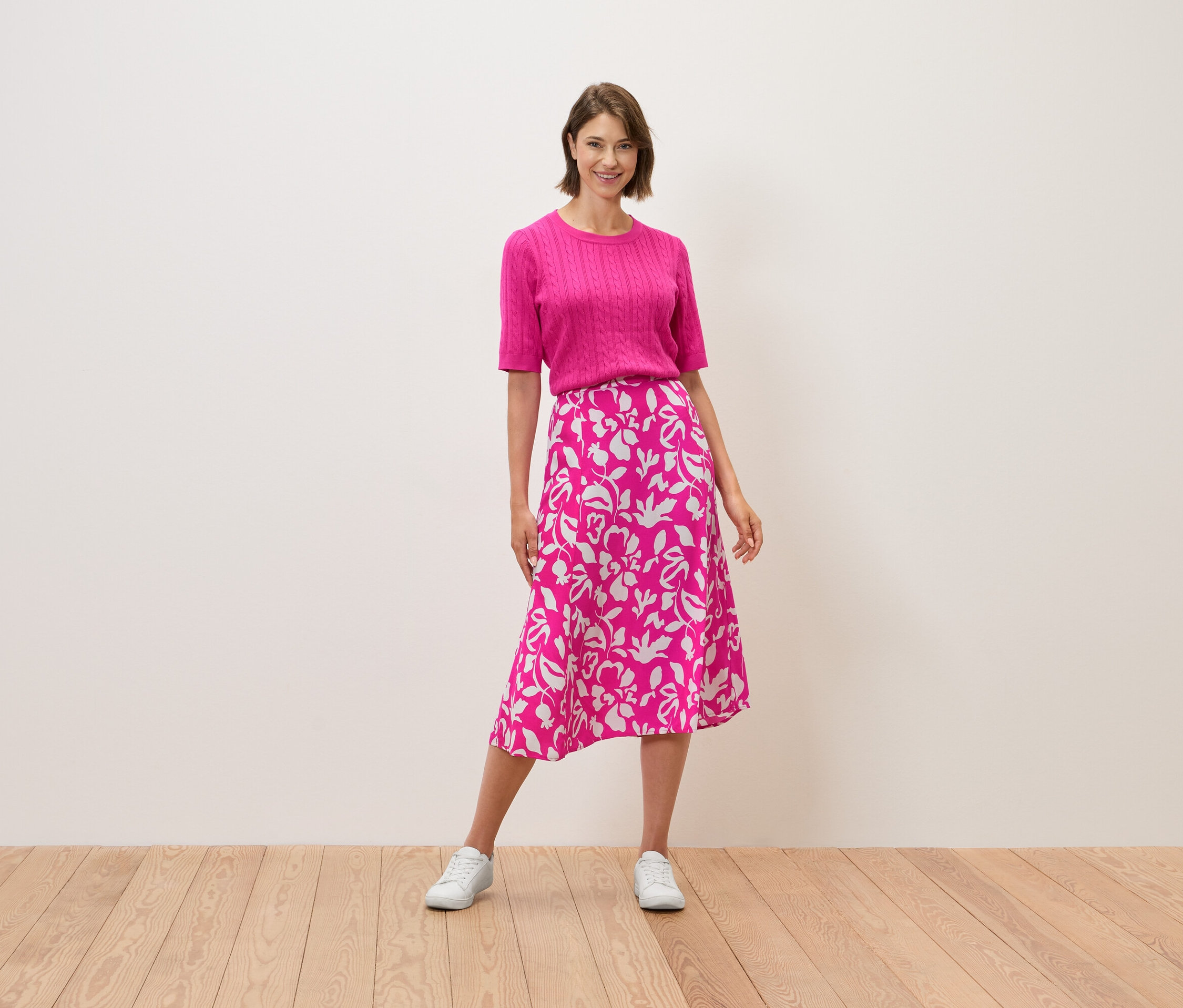 Kobieta stoi, ubrana w różowy top i spódnicę we wzory kwiatowe.