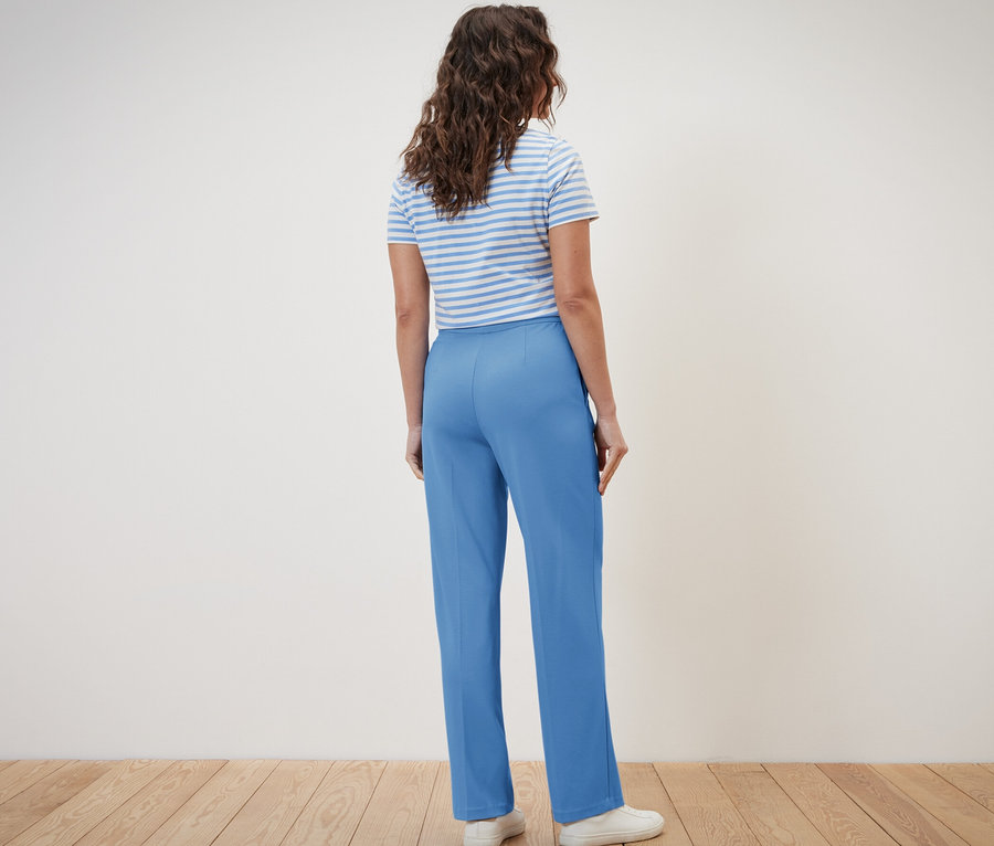 Kobieta tyłem do kamery ma na sobie niebieskie spodnie dżersejowe z kantem i koszulkę w paski.