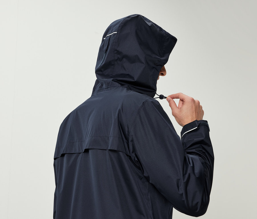 Mężczyzna w granatowej kurtce przeciwdeszczowej z kapturem ściąga sznurek kaptura.