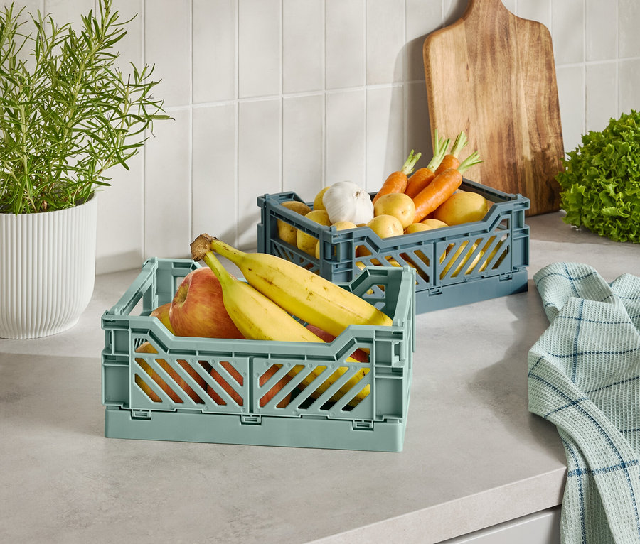 Dwa plastikowe koszyki z owocami i warzywami na blacie kuchennym.