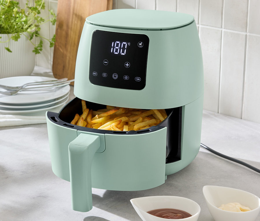 Jasnozielona frytkownica beztłuszczowa o pojemności 2 l stoi na blacie kuchennym, wypełniona frytkami. Przed nią stoją dwie miseczki z sosami.