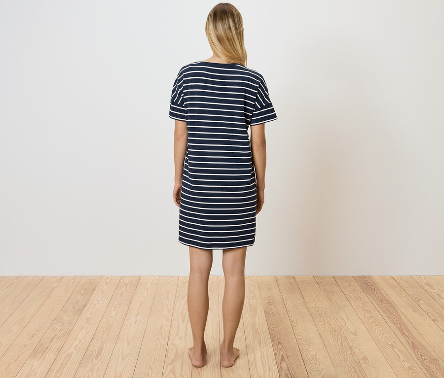 Kobieta stoi tyłem do aparatu, ubrana w granatowo-białą sukienkę w paski.