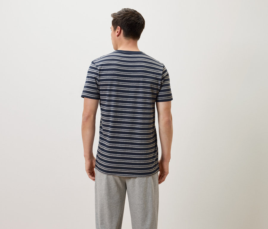 Mężczyzna od tyłu w niebiesko-szarym T-shircie w paski i szarych spodniach dresowych.