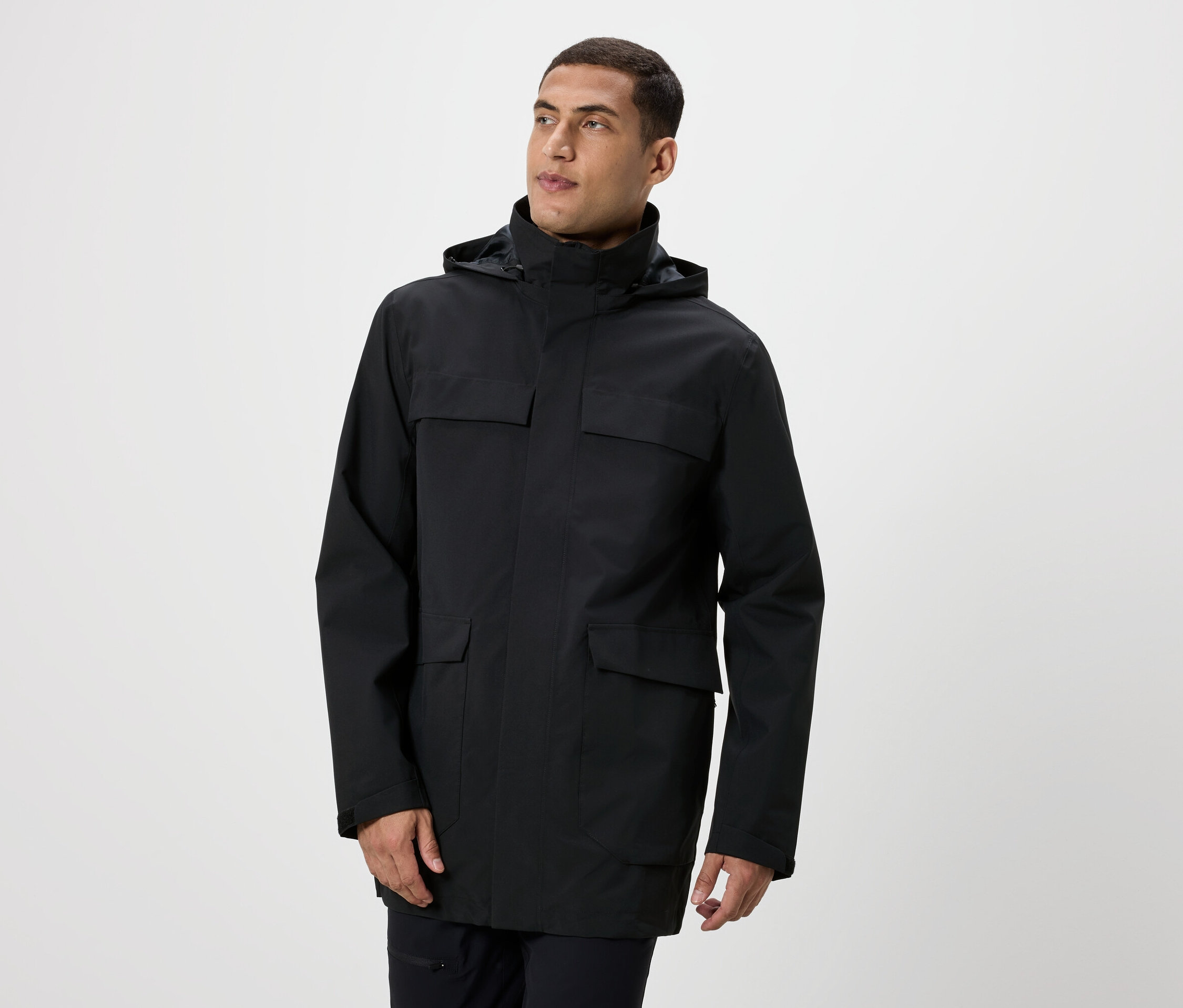 Mężczyzna pozuje w czarnej kurtce z kapturem i kieszeniami.