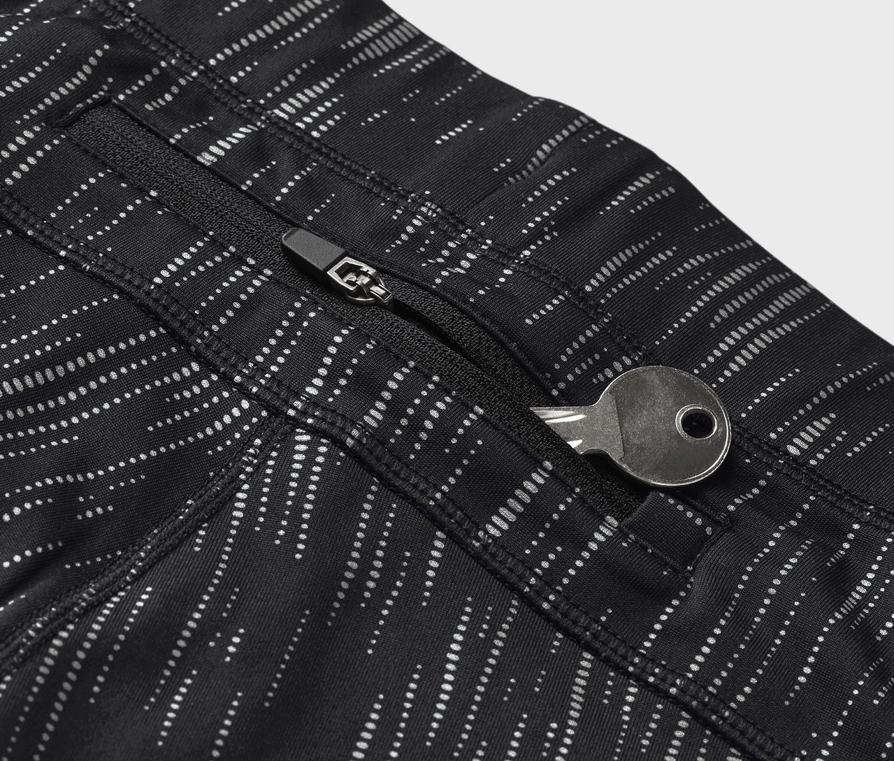 Szczegół czarnych legginsów we wzory z kluczem w kieszeni na zamek błyskawiczny.