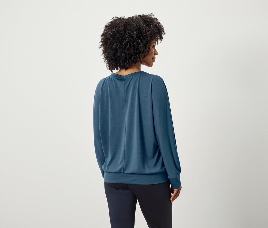 Widok z tyłu kobiety z fryzurą afro w niebieskiej bluzce z długim rękawem i granatowych spodniach.