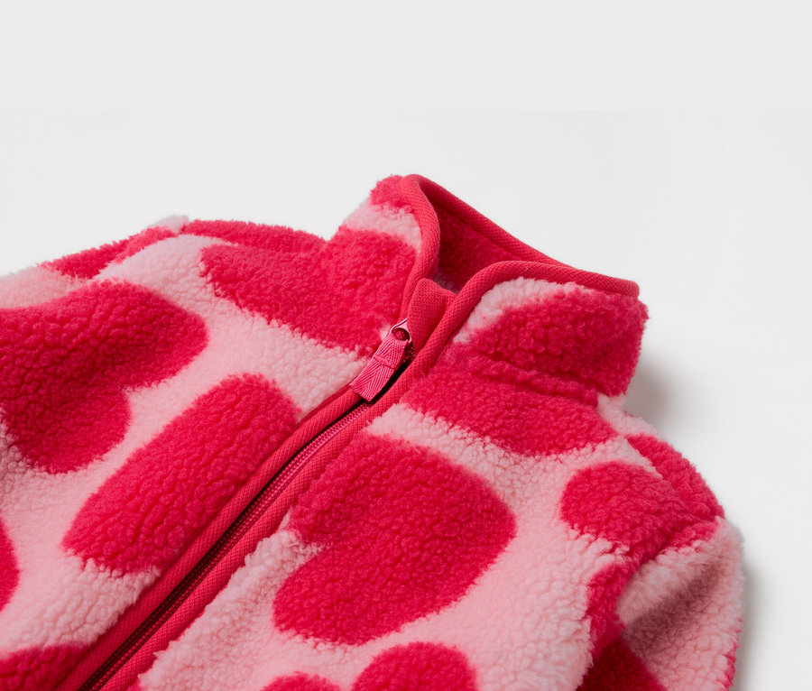 Szczegół różowej bluzy polarowej z zamkiem błyskawicznym i wzorem w serca.