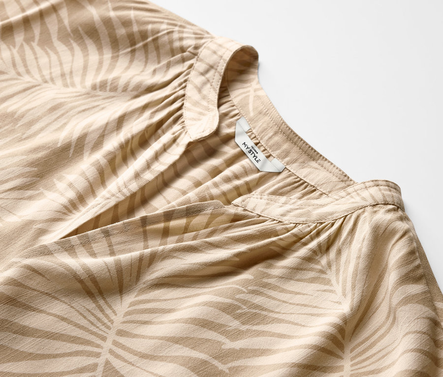 Zbliżenie na beżową bluzkę z krótkim rękawem w roślinny wzór.