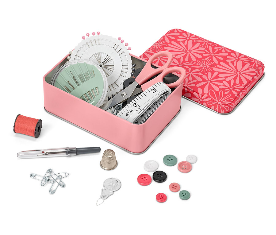Otwarty metalowy pojemnik z zestawem do szycia, obok szpulka nici, naparstek, szpilki, guziki i nawlekacz do igieł.