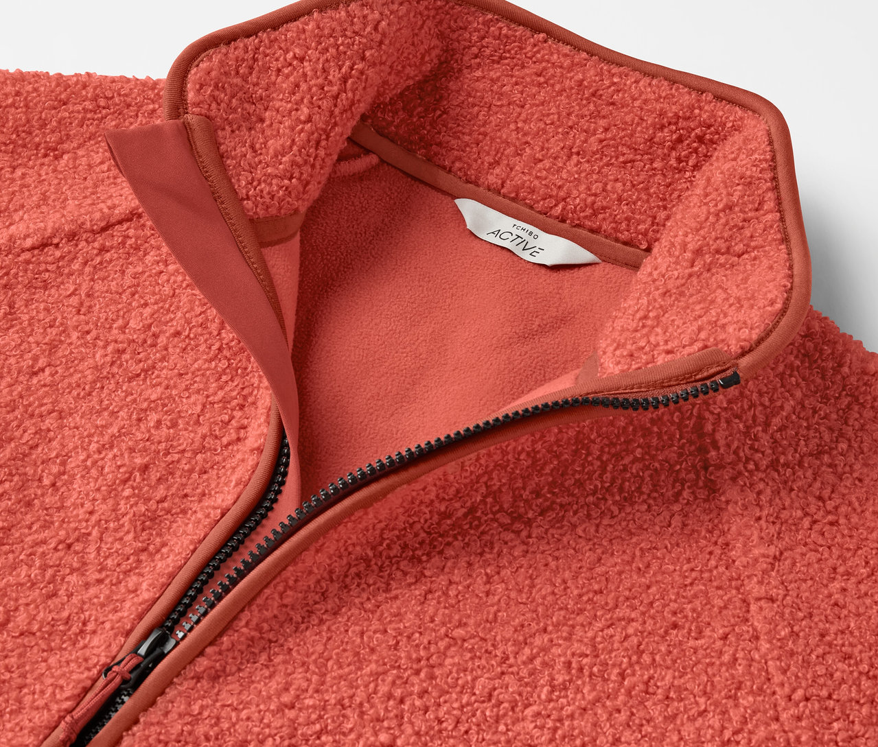 Szczegółowy widok koralowej bluzy polarowej zapinanej na zamek.