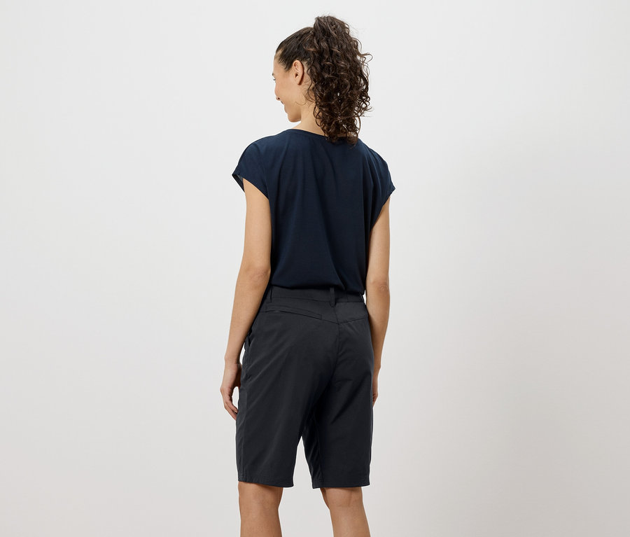 Widok z tyłu kobiety z kręconymi włosami, ubranej w granatowy T-shirt i szorty.