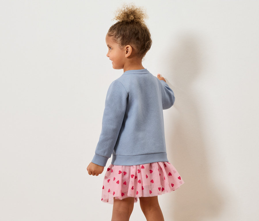 Dziewczynka od tyłu w niebieskim swetrze i różowej spódniczce w serduszka.