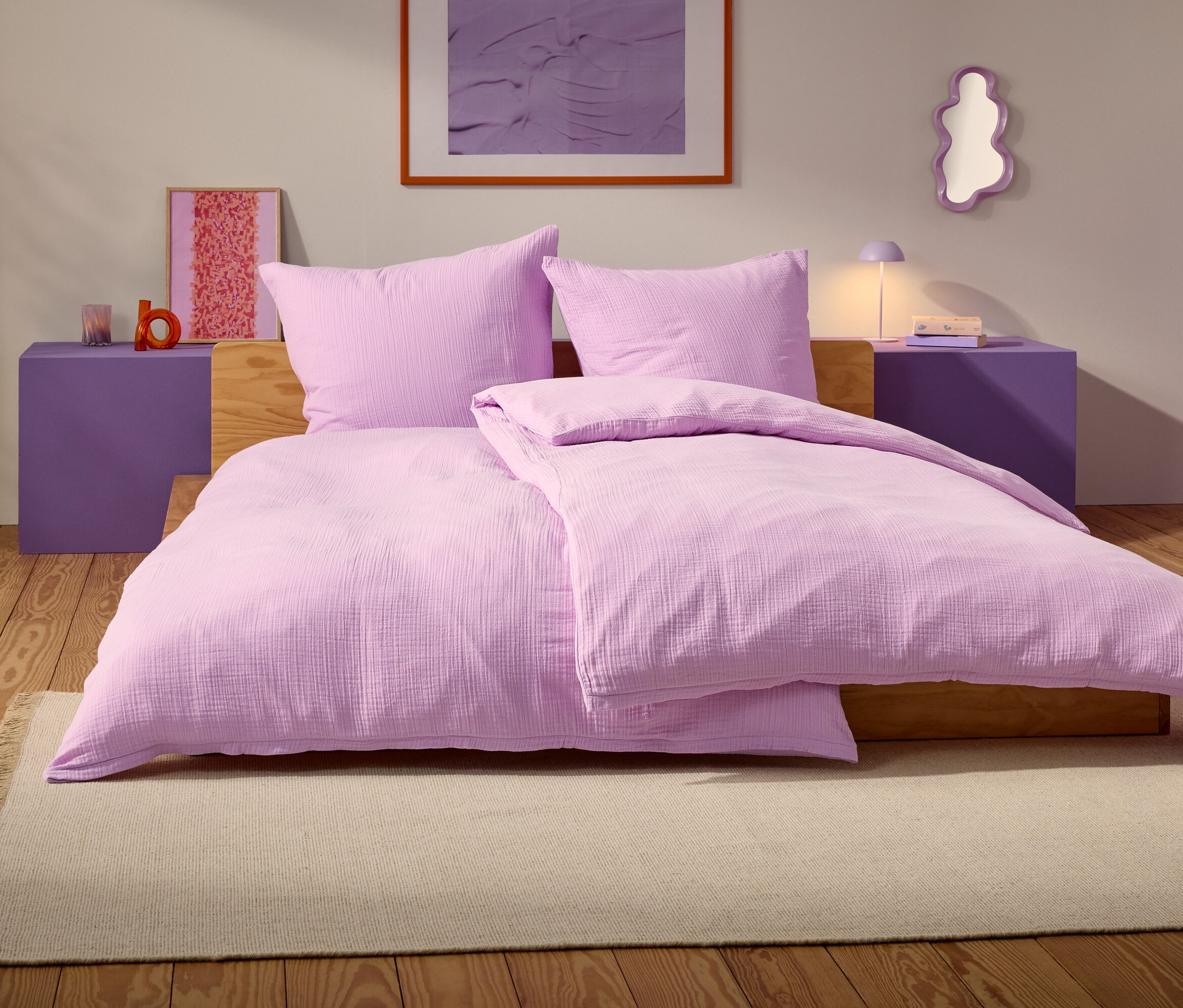 Fioletowe łóżko z dwiema poduszkami i kocem stoi na beżowym dywanie w sypialni.