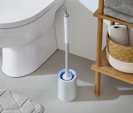 W łazience biała toaleta stoi obok szczotki do WC z niebieskim światłem i drewnianego regału z ręcznikami i papierem toaletowym.