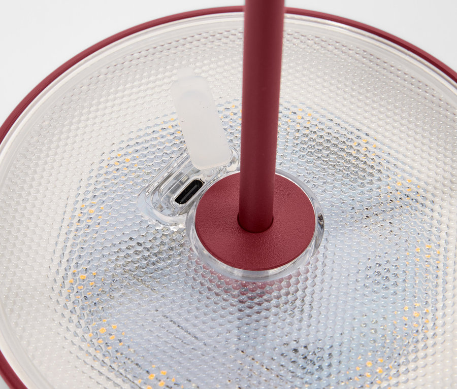 Szczegółowy widok lampy z czerwoną krawędzią i podstawką stojącej na teksturowanej powierzchni.