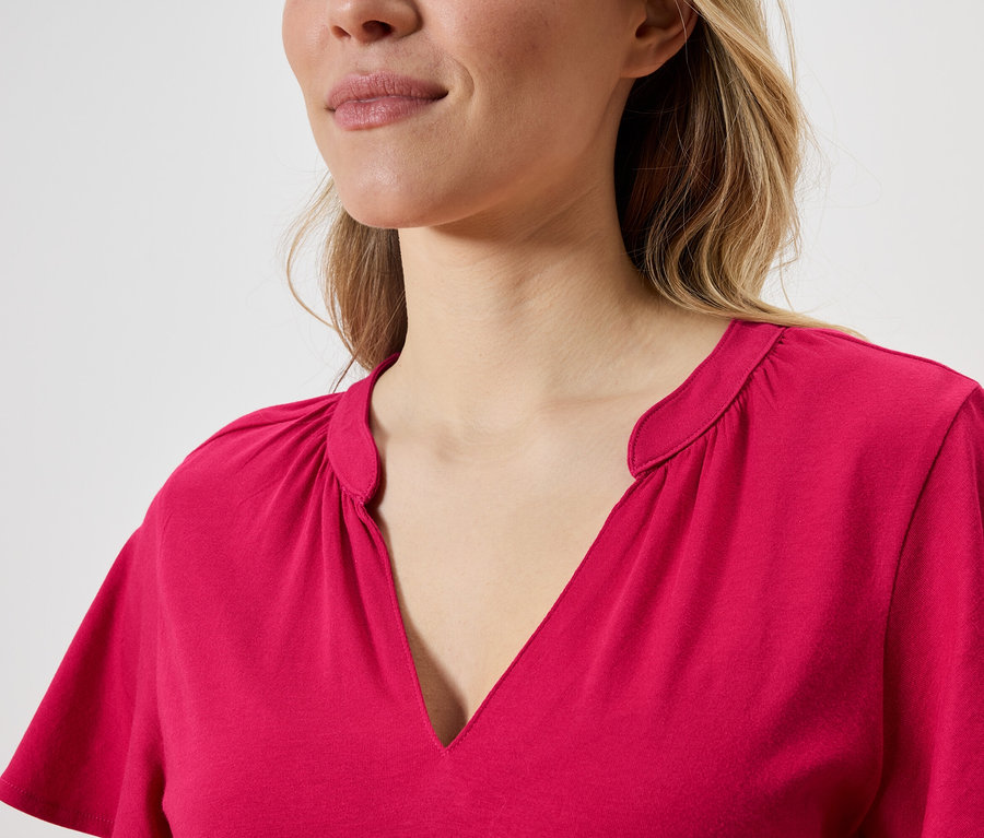 Portret kobiety o blond włosach w różowej bluzce z dekoltem w serek.
