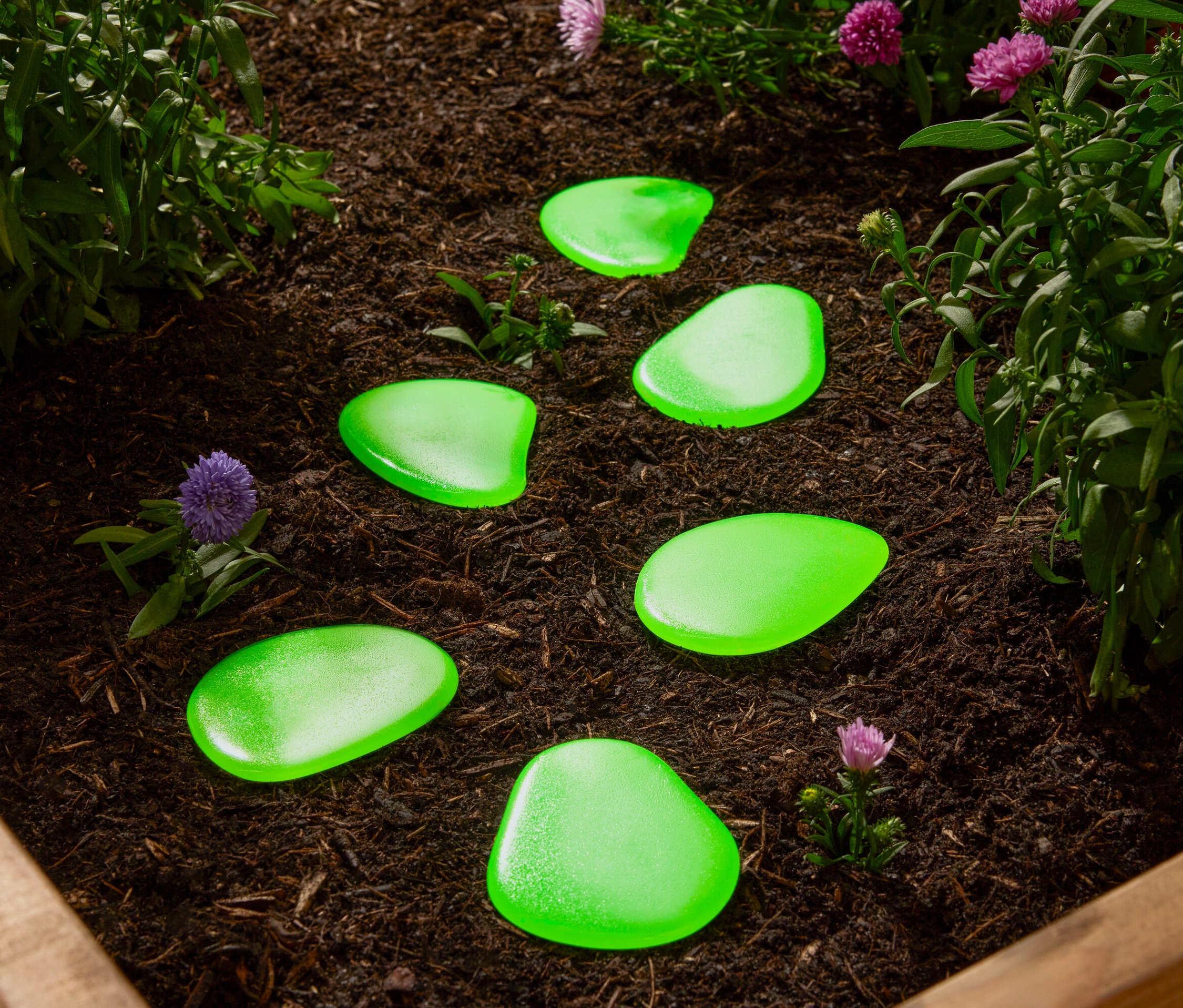 Zielone kamienie dekoracyjne leżą na rabacie wśród roślin.