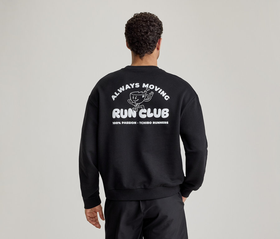 Mężczyzna od tyłu w czarnej bluzie z białym nadrukiem 'ALWAYS MOVING RUN CLUB' i biegnącą filiżanką kawy na plecach.