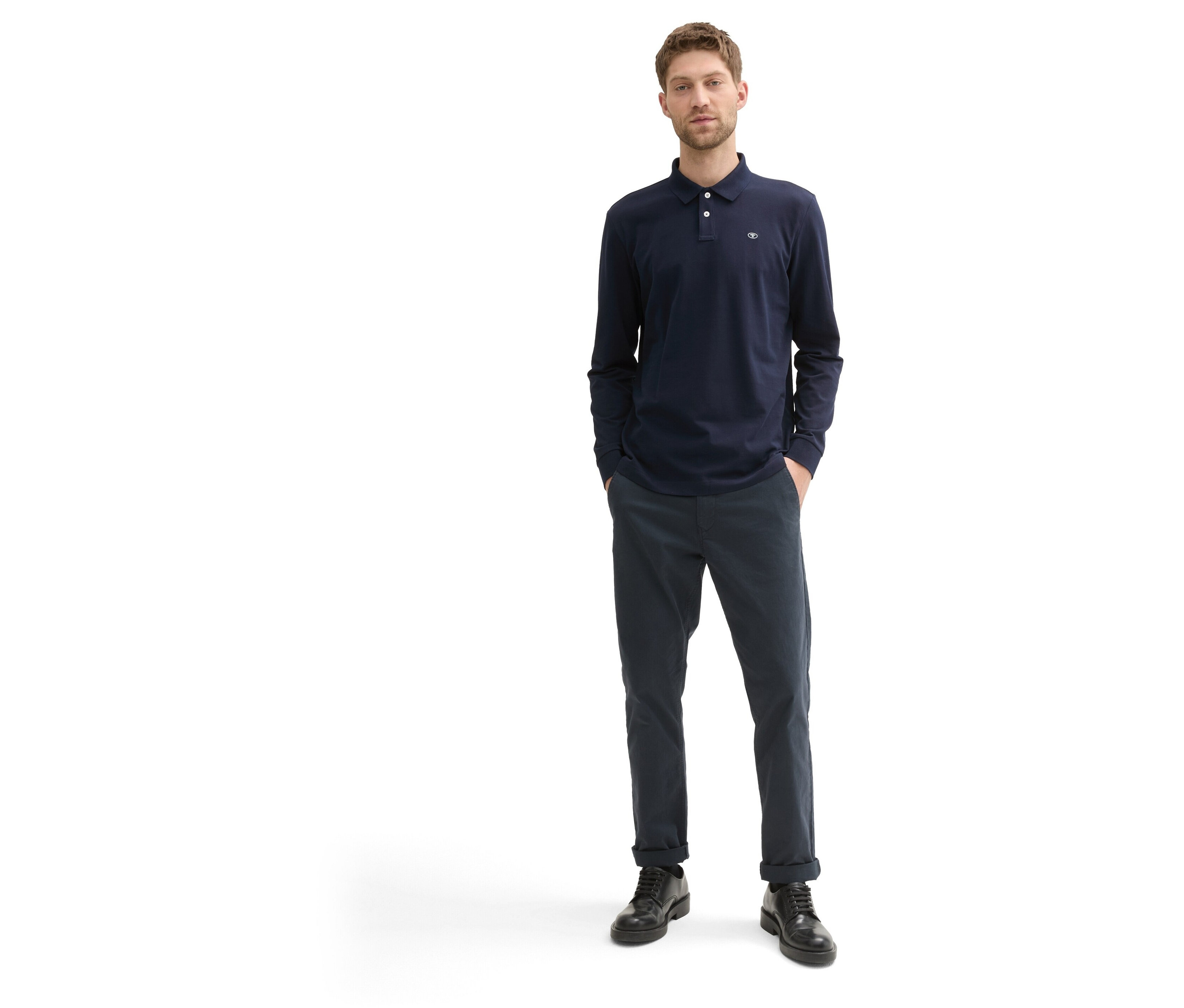 Mężczyzna stoi ubrany w granatową koszulkę polo z długim rękawem, granatowe spodnie i czarne buty.