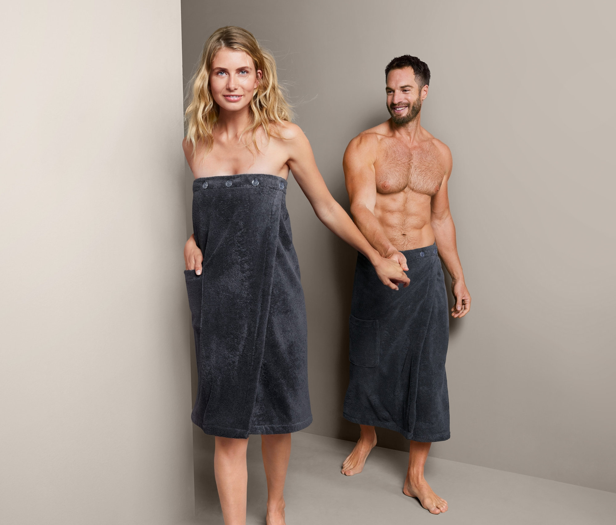 Kobieta i mężczyzna trzymają się za ręce, oboje mają na sobie szlafrok unisex do sauny z bawełny ekologicznej.