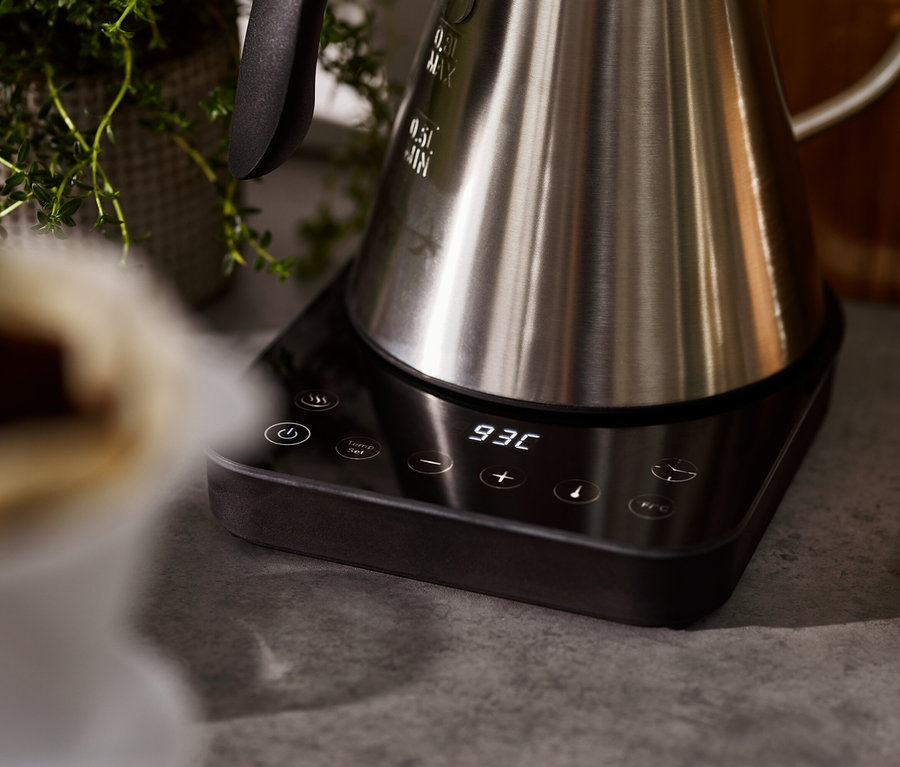 Zbliżenie na elektryczny czajnik typu konewka ze stali nierdzewnej, stojący na czarnej podstawie z cyfrowym wyświetlaczem.