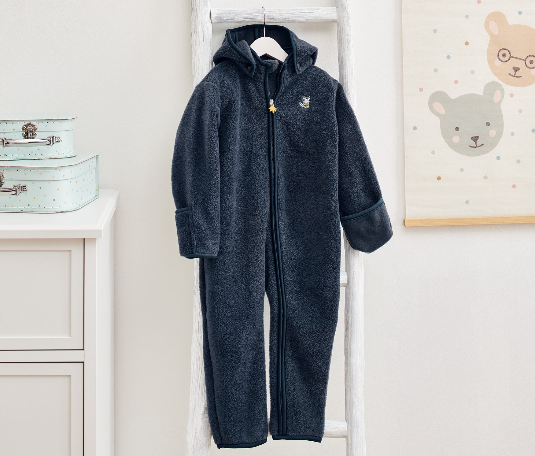Granatowy kombinezon polarowy wisi na białej drabinie w pokoju dziecięcym.