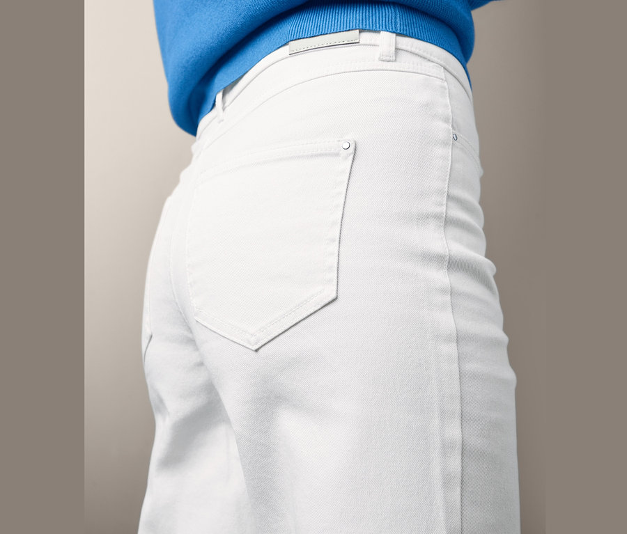 Zbliżenie na kobietę w dżinsowych spodniach typu culottes i niebieskim swetrze.