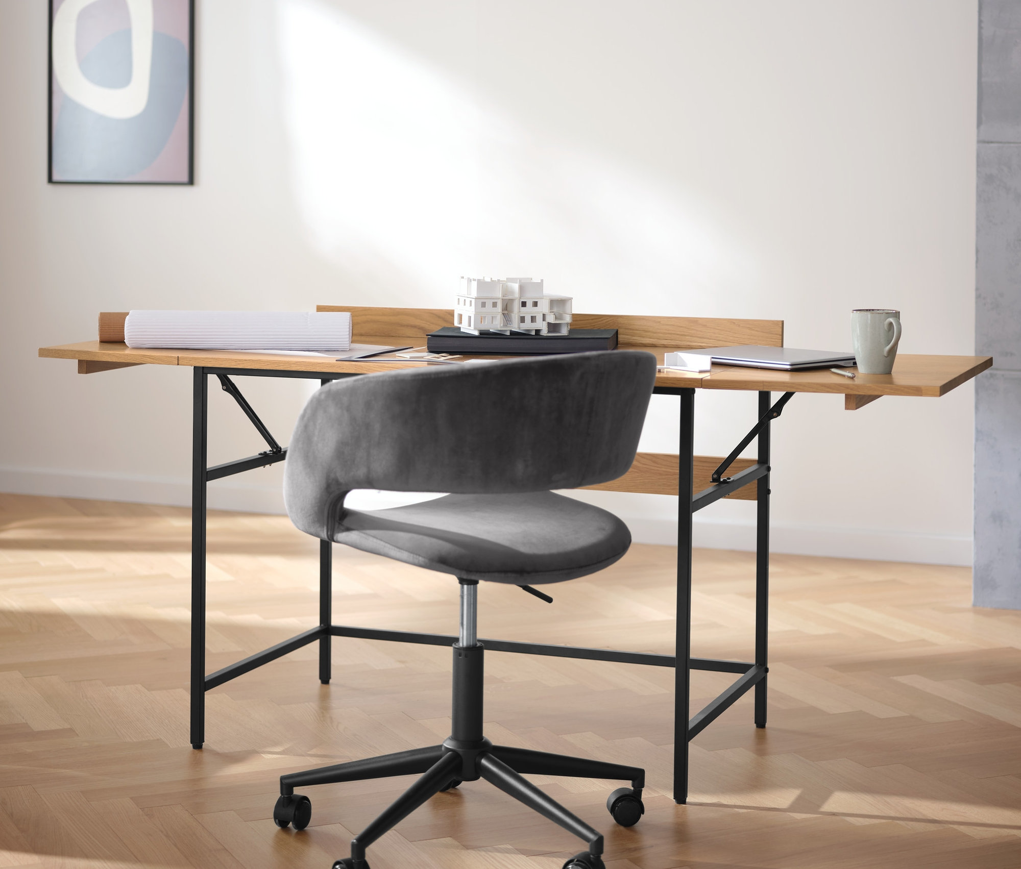 Czarna skrzynia na rośliny stoi obok lampki stołowej z metalu i biurka z litego drewna z możliwością rozbudowy.