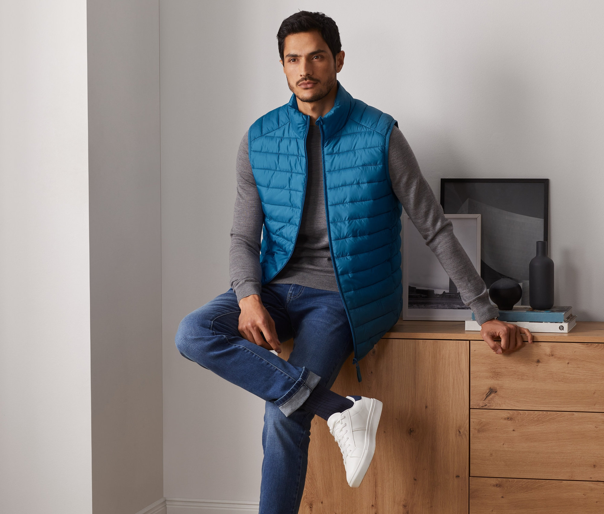 Mężczyzna siedzi na komodzie i ma na sobie kamizelkę pikowaną.