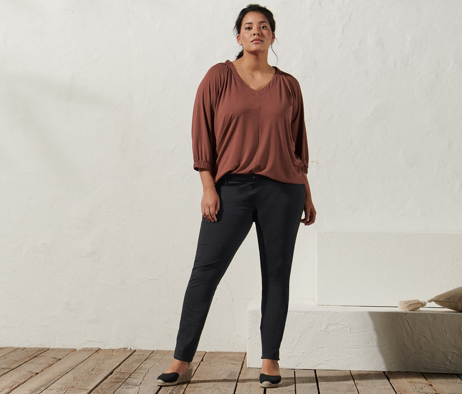 Kobieta pozuje w koszulce w kolorze terakoty z marszczeniem, jegginsach i espadrylach na koturnie.