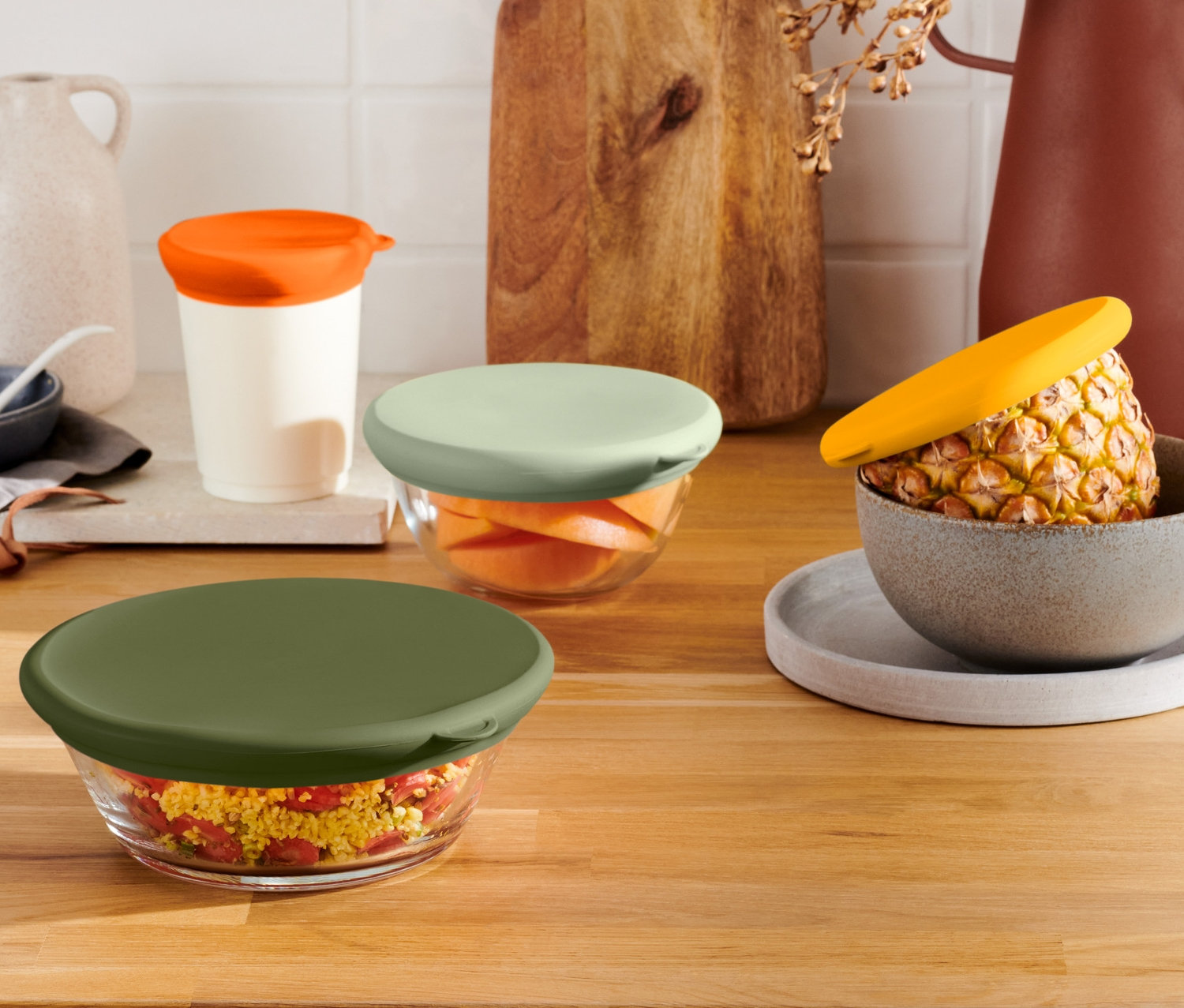 Cztery szklane miski z silikonowymi pokrywkami do utrzymywania świeżości produktów, 4 sztuki, w różnych kolorach stoją na drewnianej powierzchni.