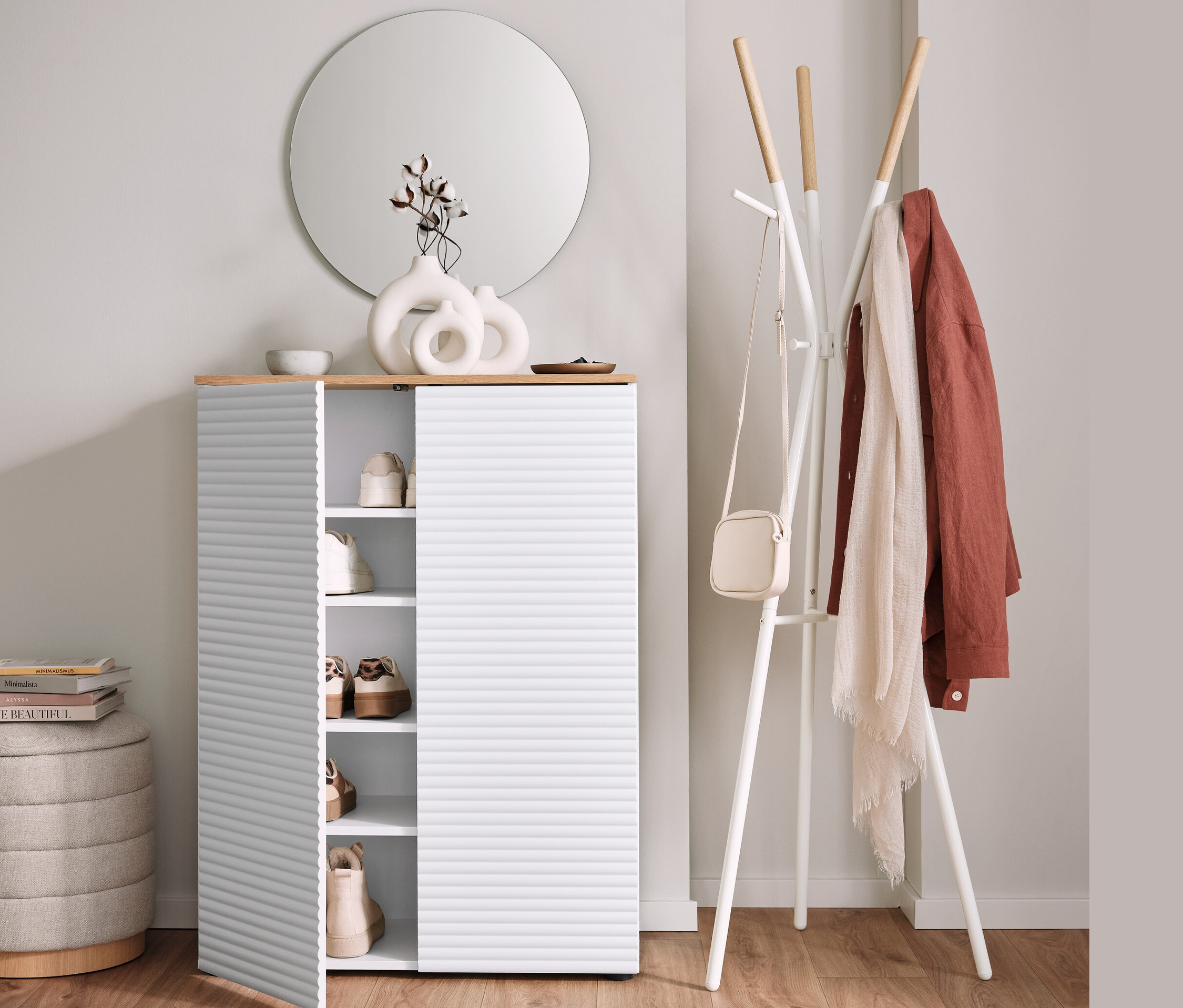 Szafka na buty z otwartymi drzwiami obok wieszaka na ubrania i pufa ze schowkiem.