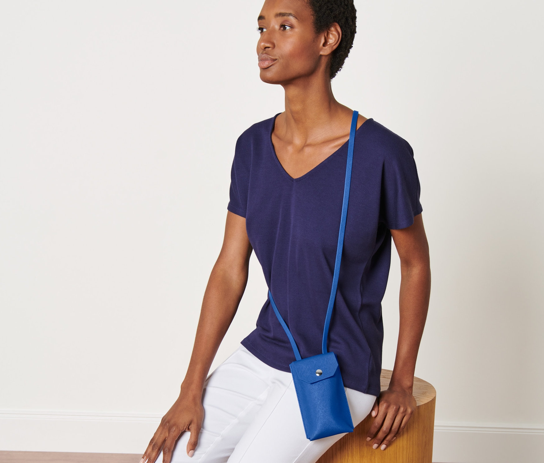 Kobieta siedzi na drewnianym stołku i ma na sobie niebieską minitorebkę.