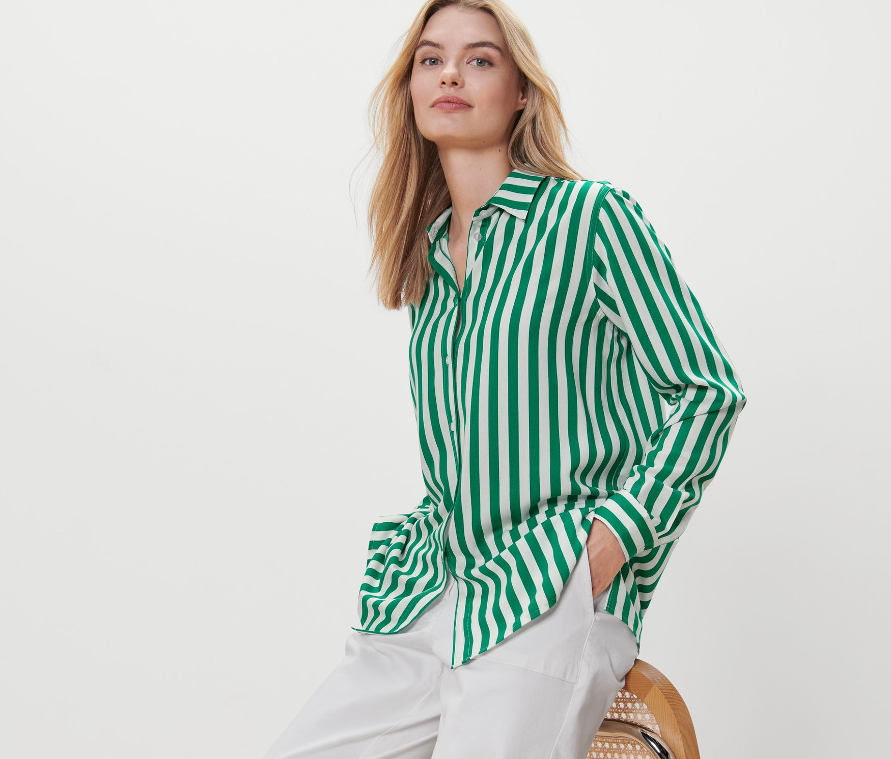 Blondwłosa kobieta siedzi na krześle, ubrana w zieloną bluzkę w paski.
