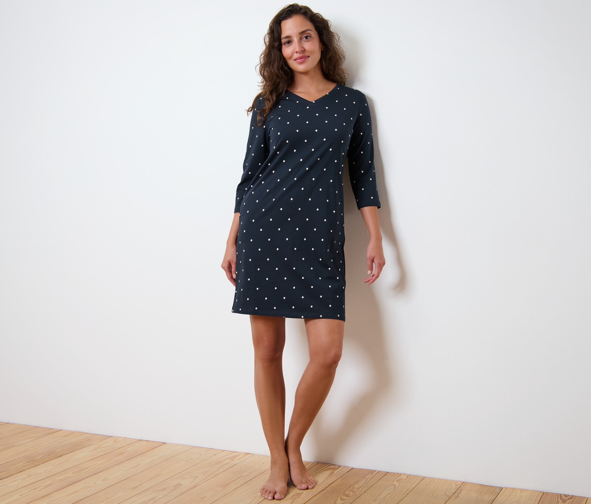 Kobieta stoi w koszuli nocnej z rękawami trzy czwarte w kropki.
