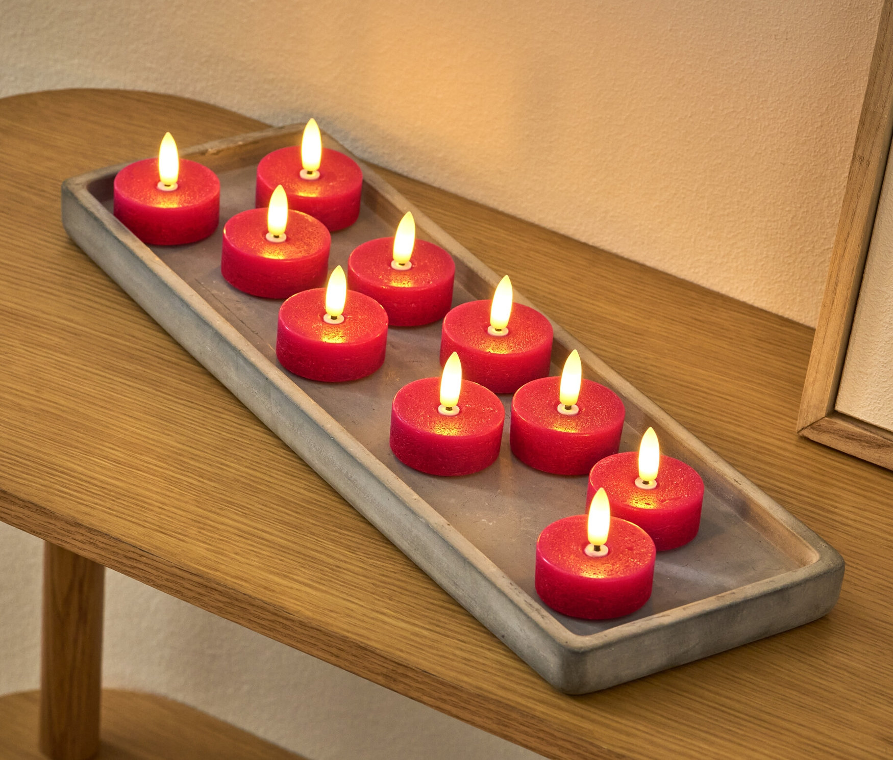 Na stole leży szara taca z dziesięcioma czerwonymi świeczkami typu tealight LED z prawdziwego wosku.