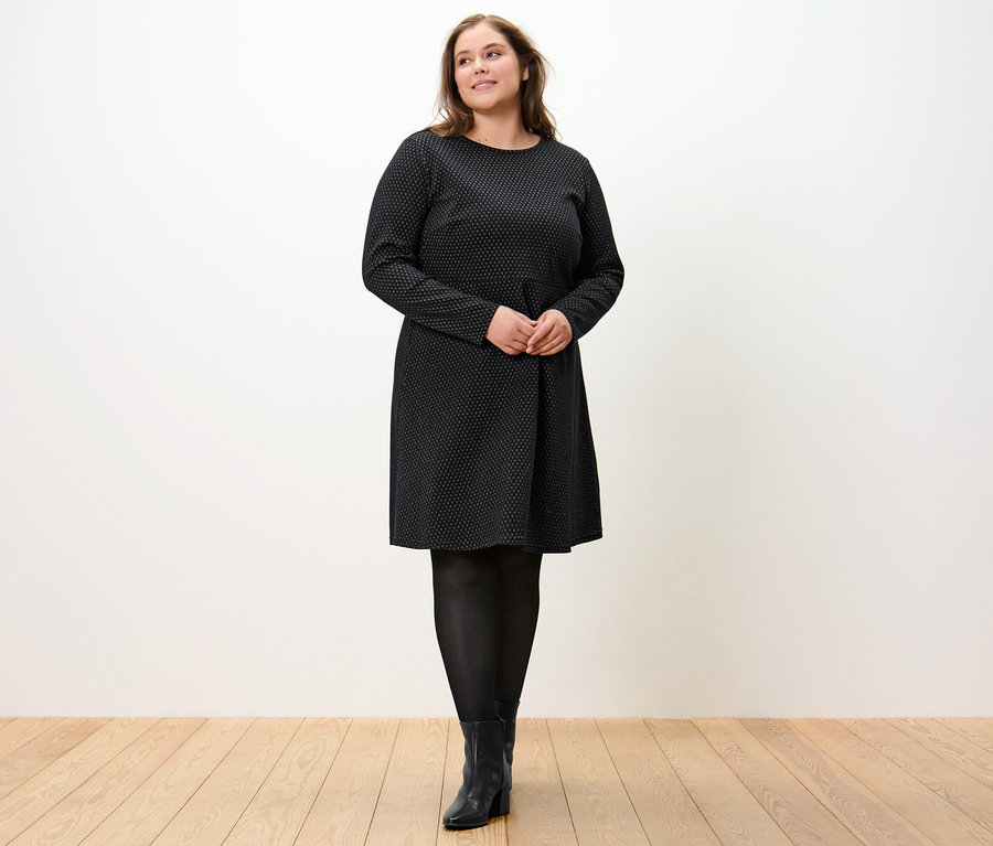 Kobieta stoi, ubrana w błyszczącą żakardową sukienkę.