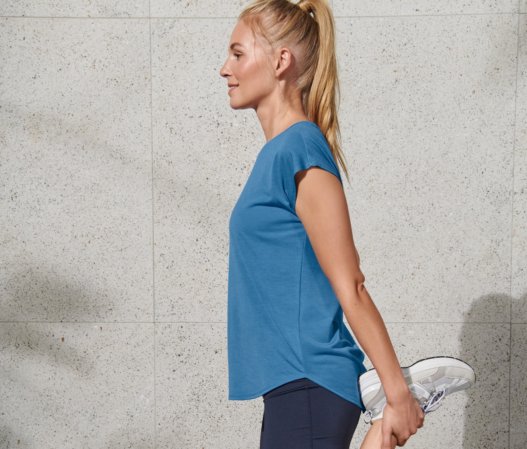 Blondynka rozciąga nogę w niebieskiej koszulce sportowej Regatta.