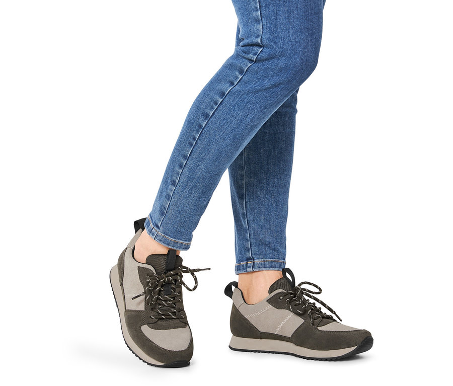Nogi w niebieskich dżinsach noszące buty typu sneakers ze skóry welurowej.