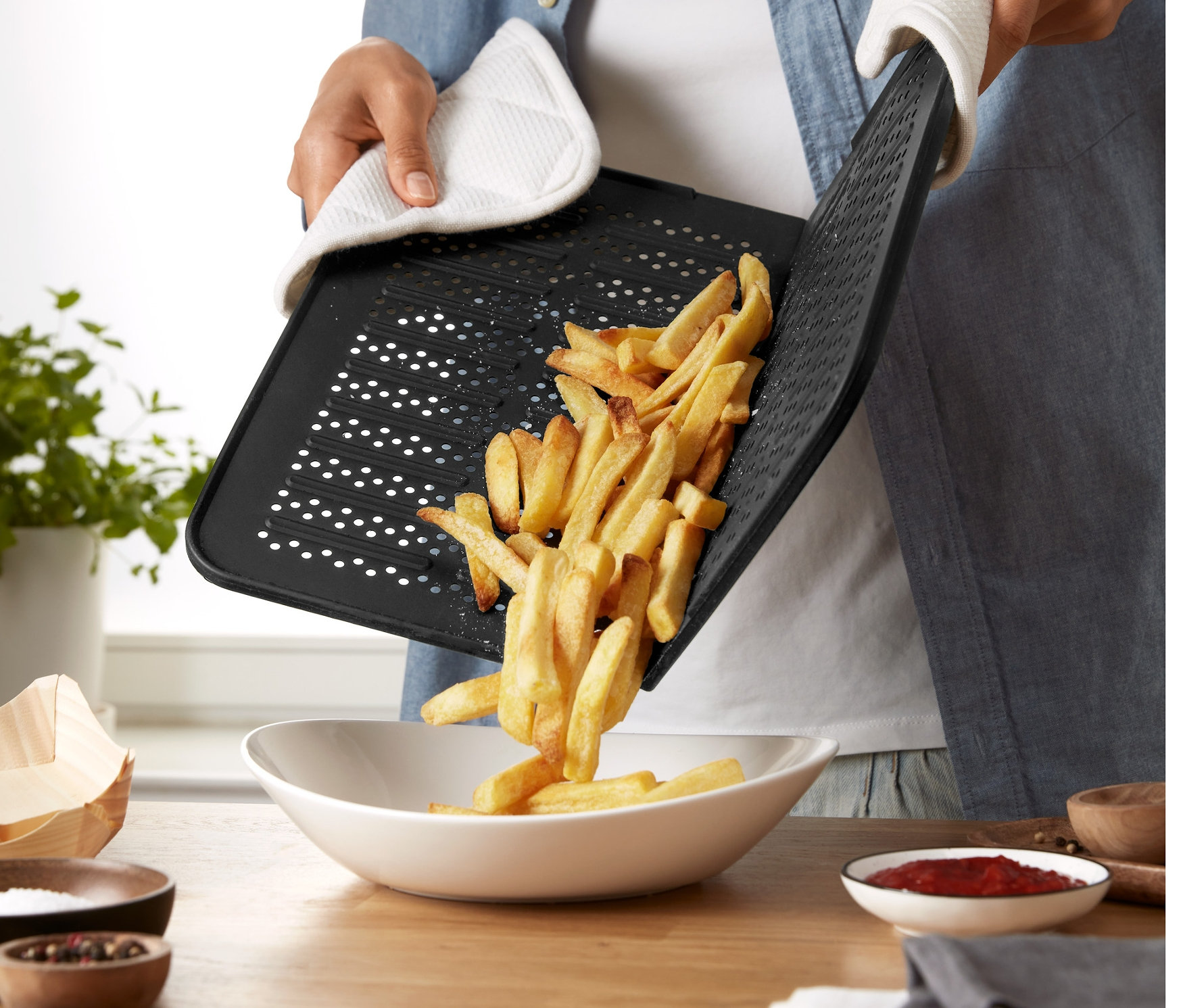 Osoba w rękawicy kuchennej przesypuje frytki z silikonowej blachy do pieczenia do miski.