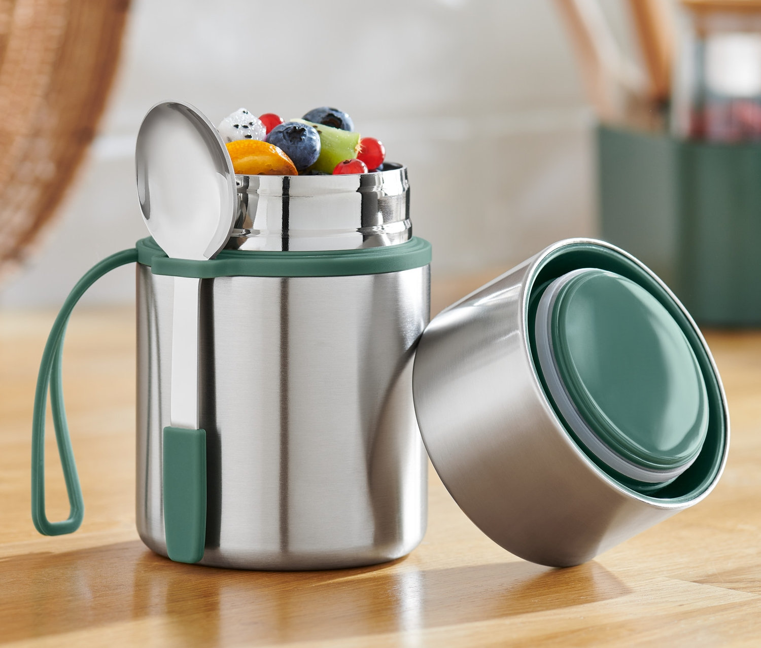 Otwarty pojemnik termiczny z owocami i łyżką na drewnianym stole.