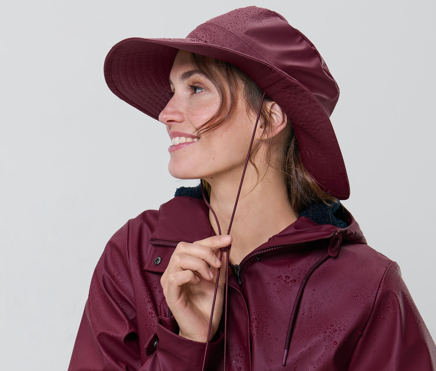 Kobieta reguluje sznurek przy bordowym kapeluszu przeciwdeszczowym.